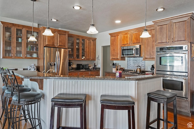 3173 N 1050 W, Pleasant View, UT 84414 - kitchen with a breakfast bar, appliances with stainless steel finishes, dark wood finished floors, glass insert cabinets, and brown cabinetry