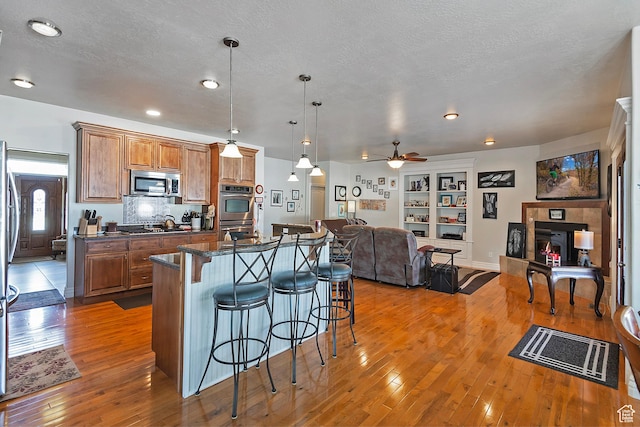 3173 N 1050 W, Pleasant View, UT 84414 - kitchen featuring a kitchen breakfast bar, brown cabinets, stainless steel appliances, ceiling fan, and hardwood / wood-style floors