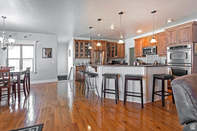 3173 N 1050 W, Pleasant View, UT 84414 - kitchen featuring a kitchen bar, brown cabinets, stainless steel appliances, hardwood / wood-style floors, and an inviting chandelier