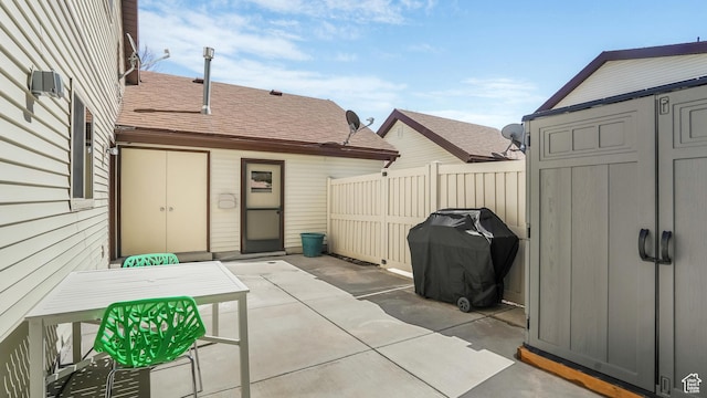 view of patio featuring an outbuilding, fence, outdoor dining space, a storage unit, and grilling area