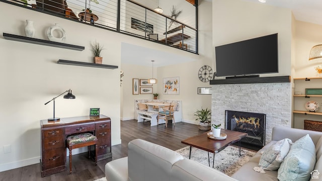 living area featuring a high ceiling, a stone fireplace, baseboards, and wood finished floors