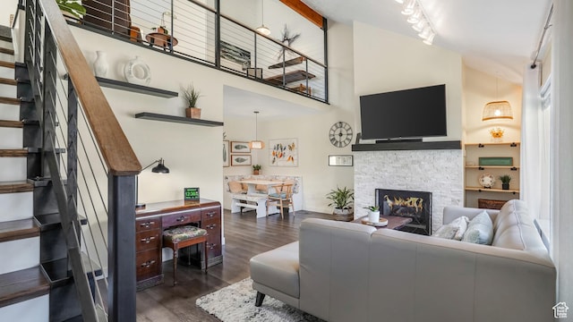 living room featuring high vaulted ceiling, stairway, wood finished floors, a stone fireplace, and rail lighting