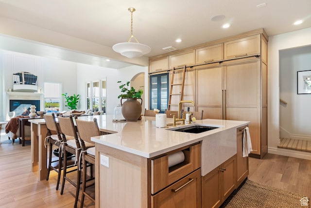 kitchen featuring a breakfast bar, a center island with sink, a sink, light wood-style floors, and open floor plan