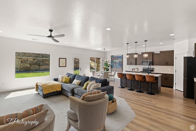 living area with a ceiling fan, recessed lighting, a textured ceiling, and light wood-type flooring