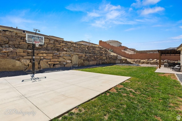 view of basketball court featuring a lawn, fence, and basketball hoop