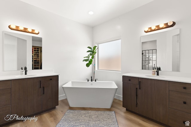 full bath with a sink, a soaking tub, two vanities, and wood finished floors