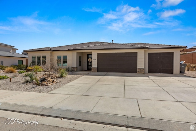 prairie-style house featuring stone siding, a tile roof, concrete driveway, and an attached garage
