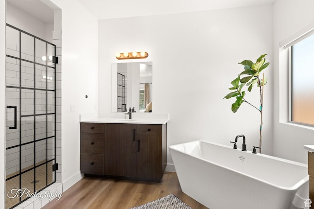 full bathroom with vanity, baseboards, a stall shower, a freestanding bath, and wood finished floors