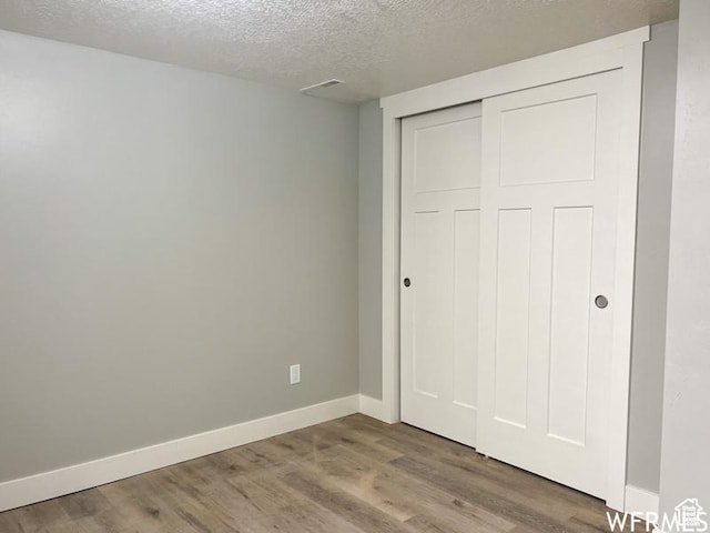 unfurnished bedroom featuring a textured ceiling, wood finished floors, a closet, and baseboards