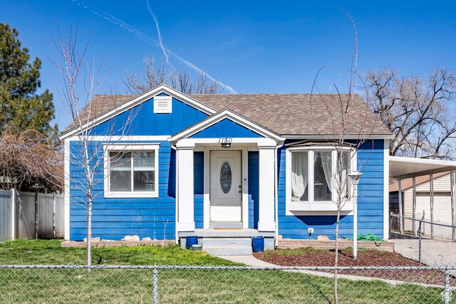 view of front facade with an attached carport, fence, a front lawn, and roof with shingles