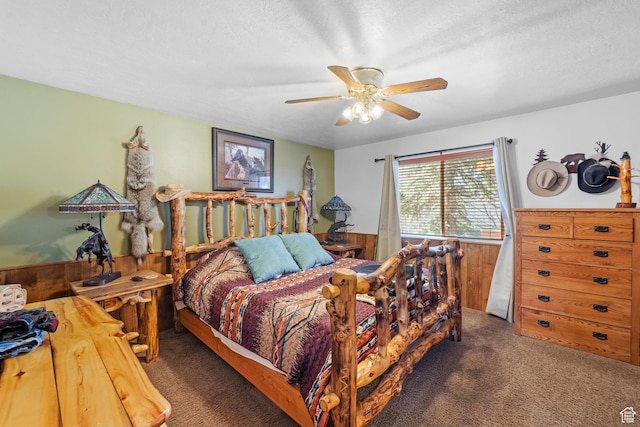 bedroom with wood walls, carpet flooring, a textured ceiling, a wainscoted wall, and a ceiling fan