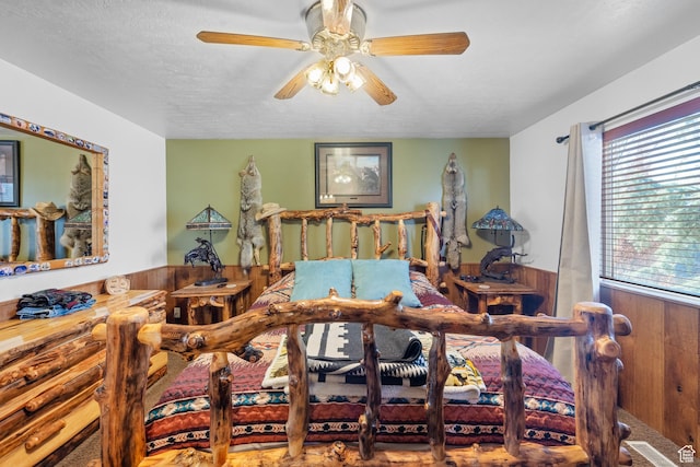 bedroom featuring a textured ceiling, visible vents, ceiling fan, and wainscoting