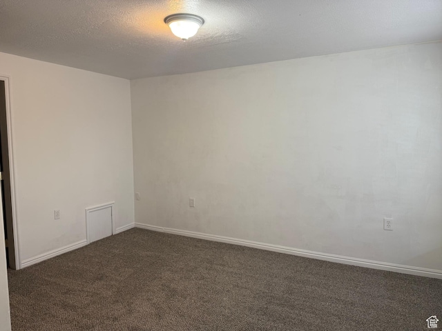 spare room featuring dark carpet, a textured ceiling, and baseboards