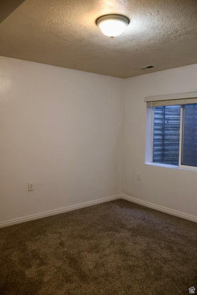 empty room with a textured ceiling, dark colored carpet, and baseboards