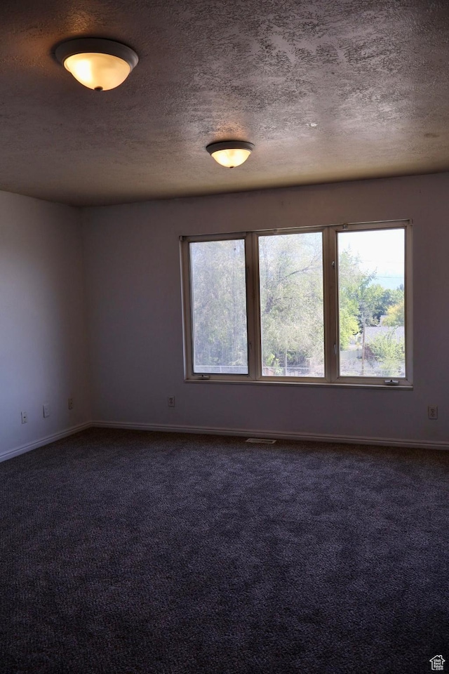 unfurnished room featuring dark carpet, baseboards, and a textured ceiling