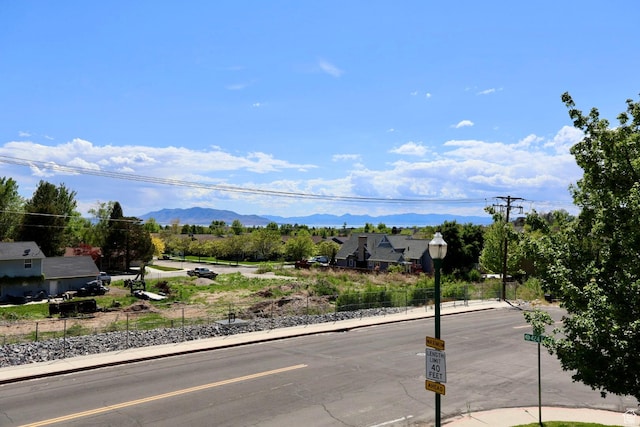 view of asphalt road featuring curbs, sidewalks, a mountain view, and street lighting