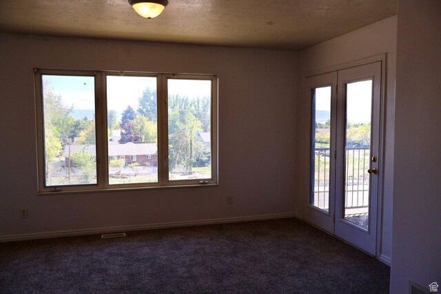 empty room featuring plenty of natural light, dark colored carpet, and baseboards