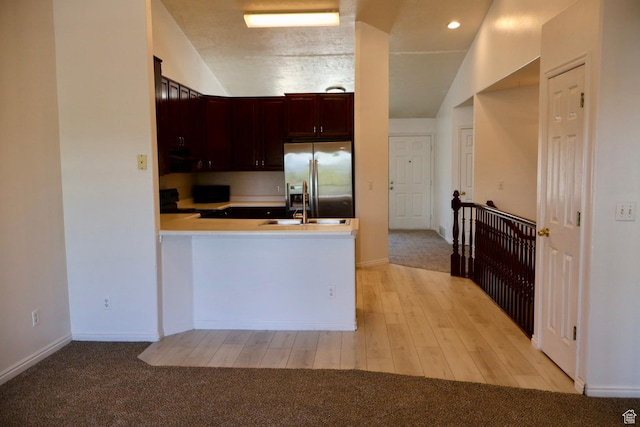 kitchen with stainless steel fridge, vaulted ceiling, light countertops, a peninsula, and black gas range