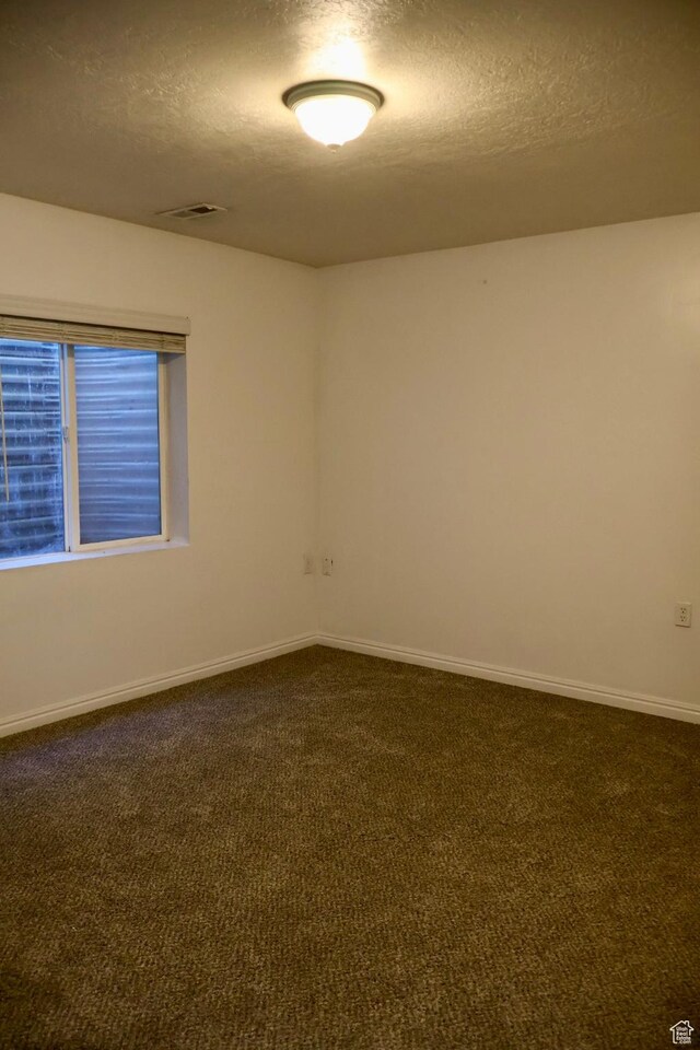 unfurnished room featuring a textured ceiling, dark carpet, and baseboards