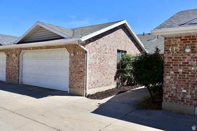 view of home's exterior with brick siding, an attached garage, concrete driveway, and a shingled roof