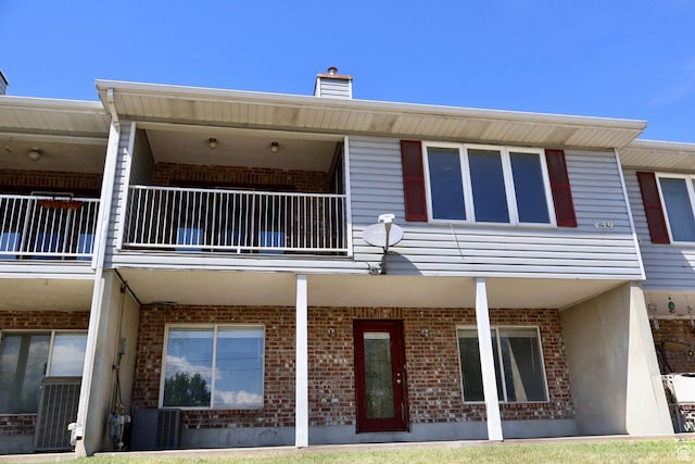 rear view of property with a balcony, brick siding, cooling unit, and a chimney
