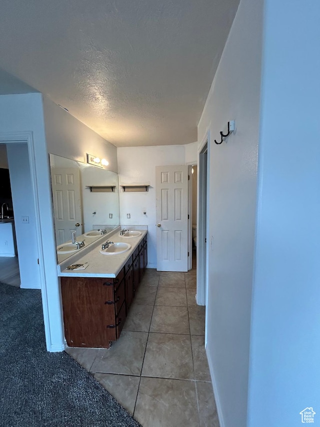 bathroom with a textured ceiling, double vanity, baseboards, and tile patterned floors