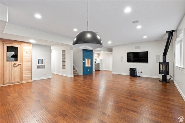 unfurnished living room with wood finished floors, stairs, a wood stove, baseboards, and recessed lighting