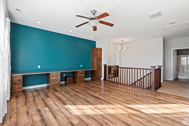 empty room with built in study area, wood finished floors, and visible vents
