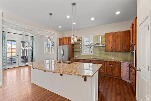 kitchen with brown cabinetry, wall chimney exhaust hood, appliances with stainless steel finishes, and dark wood-style floors
