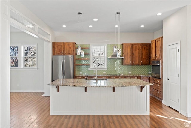 kitchen featuring stainless steel appliances, a sink, light wood-style floors, tasteful backsplash, and brown cabinetry