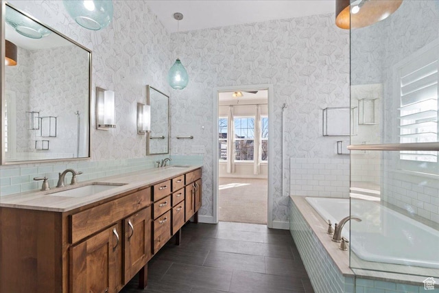 full bathroom featuring wallpapered walls, a relaxing tiled tub, a sink, and double vanity