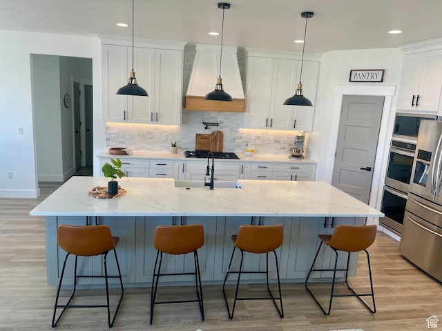 9940 N Vande Way, Eagle Mountain, UT 84005 - kitchen featuring light wood-style flooring, appliances with stainless steel finishes, white cabinetry, custom range hood, and backsplash