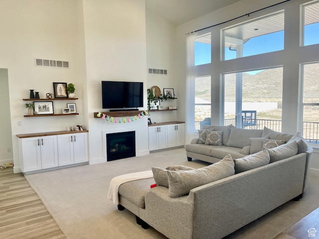 9940 N Vande Way, Eagle Mountain, UT 84005 - living area featuring visible vents, light wood-style flooring, a towering ceiling, and a fireplace