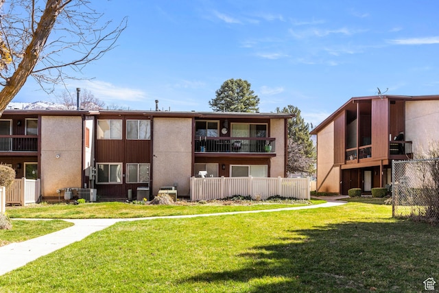 rear view of property featuring central air condition unit, a lawn, stucco siding, and fence