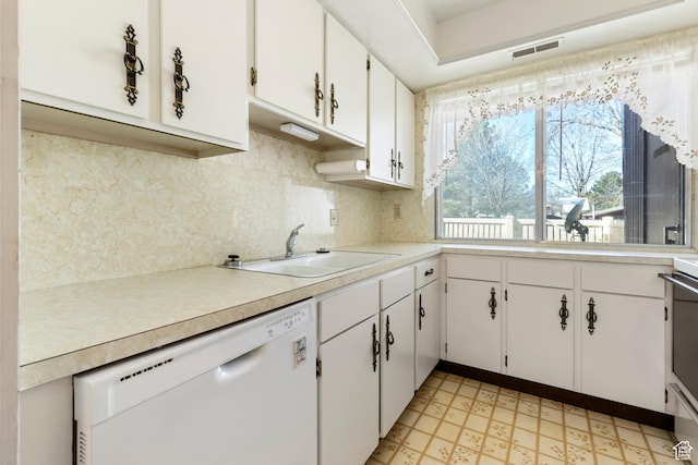 kitchen featuring light countertops, a sink, tasteful backsplash, light floors, and white dishwasher