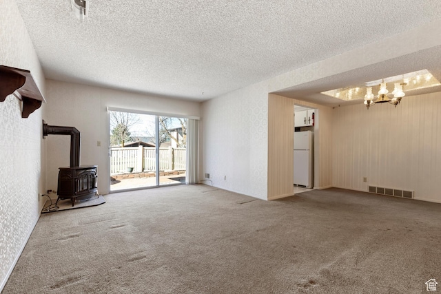 unfurnished living room featuring a notable chandelier, a wood stove, a textured ceiling, visible vents, and carpet