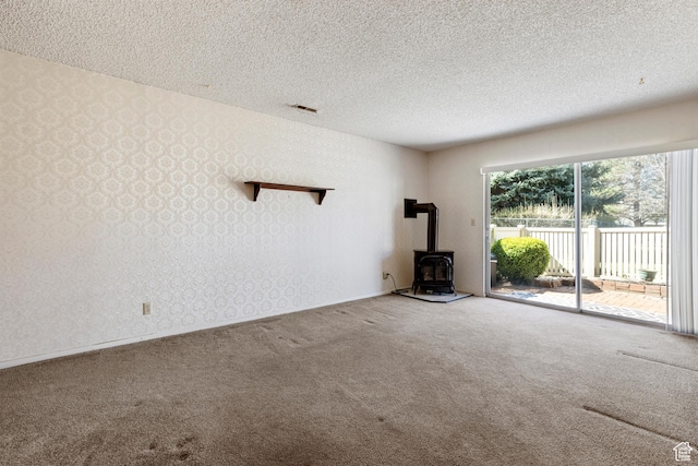 unfurnished living room with carpet floors, a textured ceiling, wallpapered walls, and a wood stove