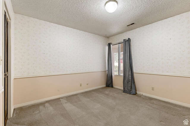 carpeted empty room featuring visible vents, a textured ceiling, wallpapered walls, and a wainscoted wall