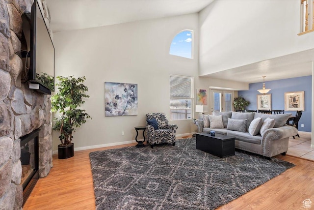 living room with a high ceiling, a stone fireplace, baseboards, and light wood finished floors