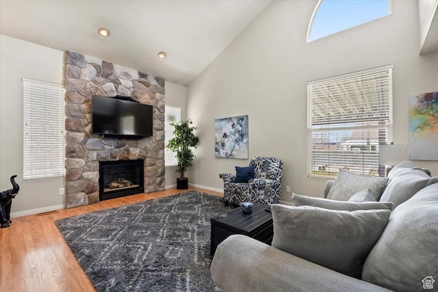 living area with high vaulted ceiling, baseboards, visible vents, a fireplace, and wood finished floors