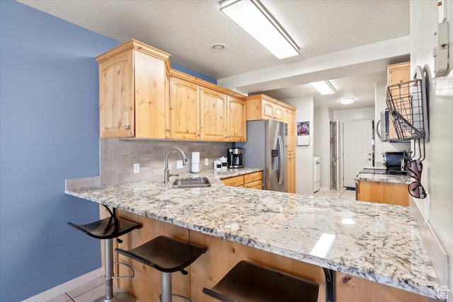 kitchen featuring light stone counters, backsplash, a sink, light brown cabinetry, and stainless steel fridge
