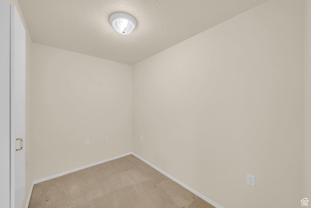 unfurnished room with light colored carpet, baseboards, and a textured ceiling