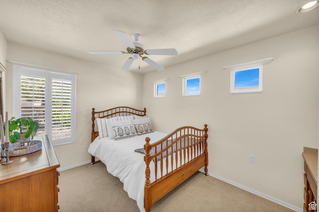bedroom with light colored carpet, baseboards, ceiling fan, and a textured ceiling