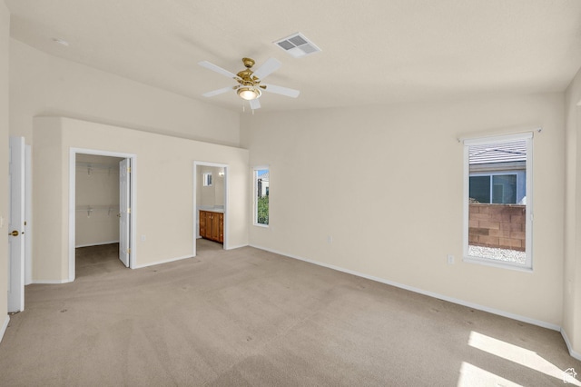 unfurnished bedroom with light colored carpet, a spacious closet, baseboards, a closet, and connected bathroom