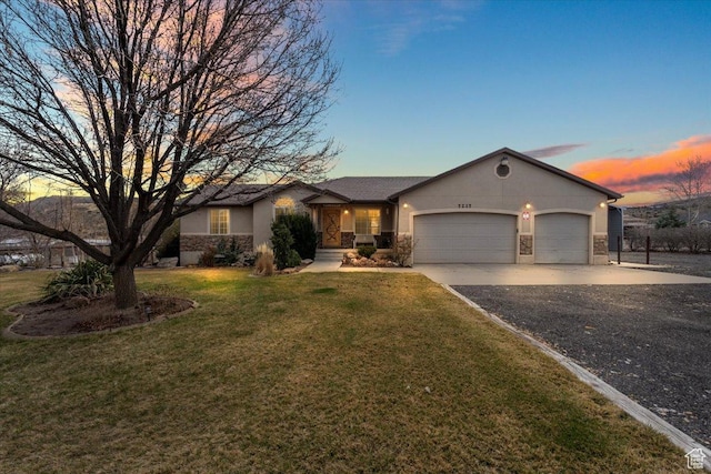 ranch-style home featuring driveway, stone siding, stucco siding, a garage, and a yard