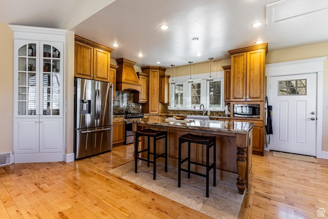2503 W State Road 32, Peoa, UT 84061 - kitchen with light wood-style flooring, custom exhaust hood, brown cabinets, appliances with stainless steel finishes, and a kitchen breakfast bar