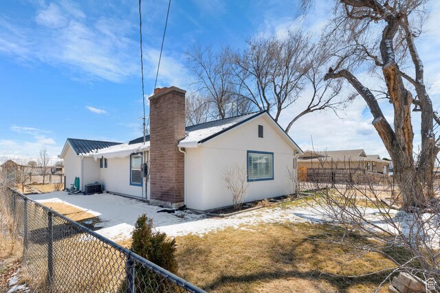 back of property with metal roof, central AC unit, a chimney, a fenced backyard, and stucco siding