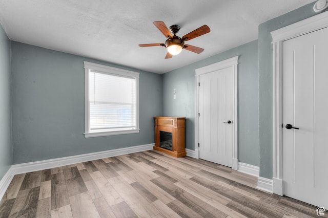 unfurnished bedroom featuring baseboards, light wood-style flooring, ceiling fan, and a glass covered fireplace
