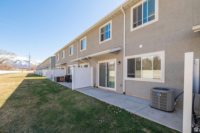 back of house featuring stucco siding, fence, a lawn, central AC, and a patio area