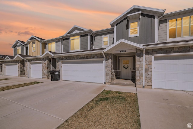 multi unit property featuring stone siding, board and batten siding, concrete driveway, and a garage